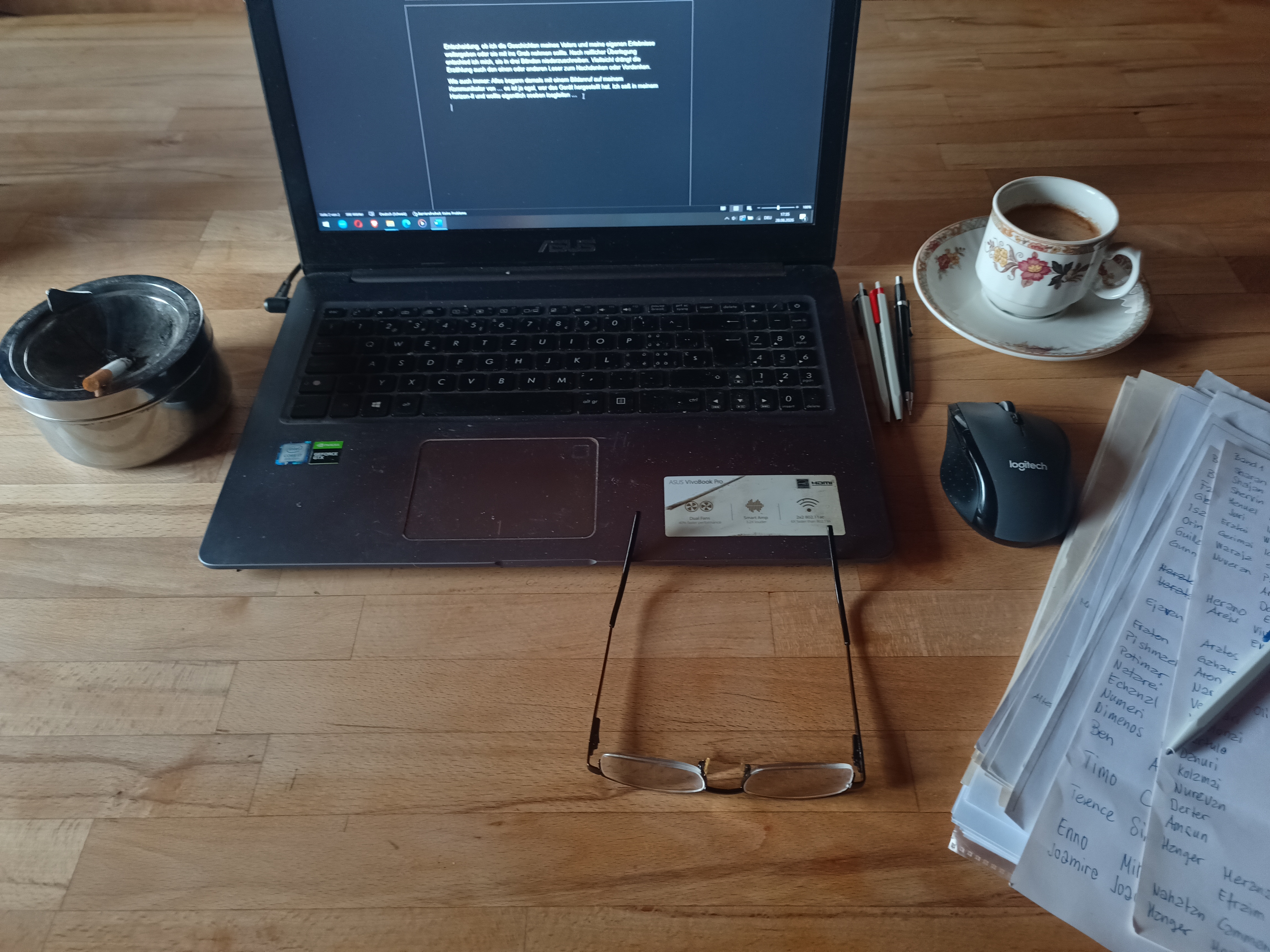Arbeitsplatz von Roland Späti: Ein Laptop mit offenem Manuskript auf einem massiven, naturbelassenen Eichentisch. Daneben ein Stapel Notizen mit den notwendigen Schreibutensilien und vier farbigen Stiften, eine Tasse Kaffee, eine Lesebrille und eine brennende Zigarette im Aschenbecher. Ein authentischer Blick in den kreativen Prozess der Tetralogie.